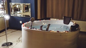 A large, freestanding bathtub with a faucet and a control panel, surrounded by candles and rose petals. - Mas Suites Karaköy (Istanbul)