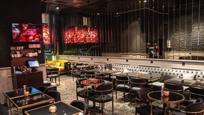 A modern restaurant with multiple tables and chairs, a bar area, and a large TV screen displaying a cosmic image. - Mas Suites Karaköy (Istanbul)