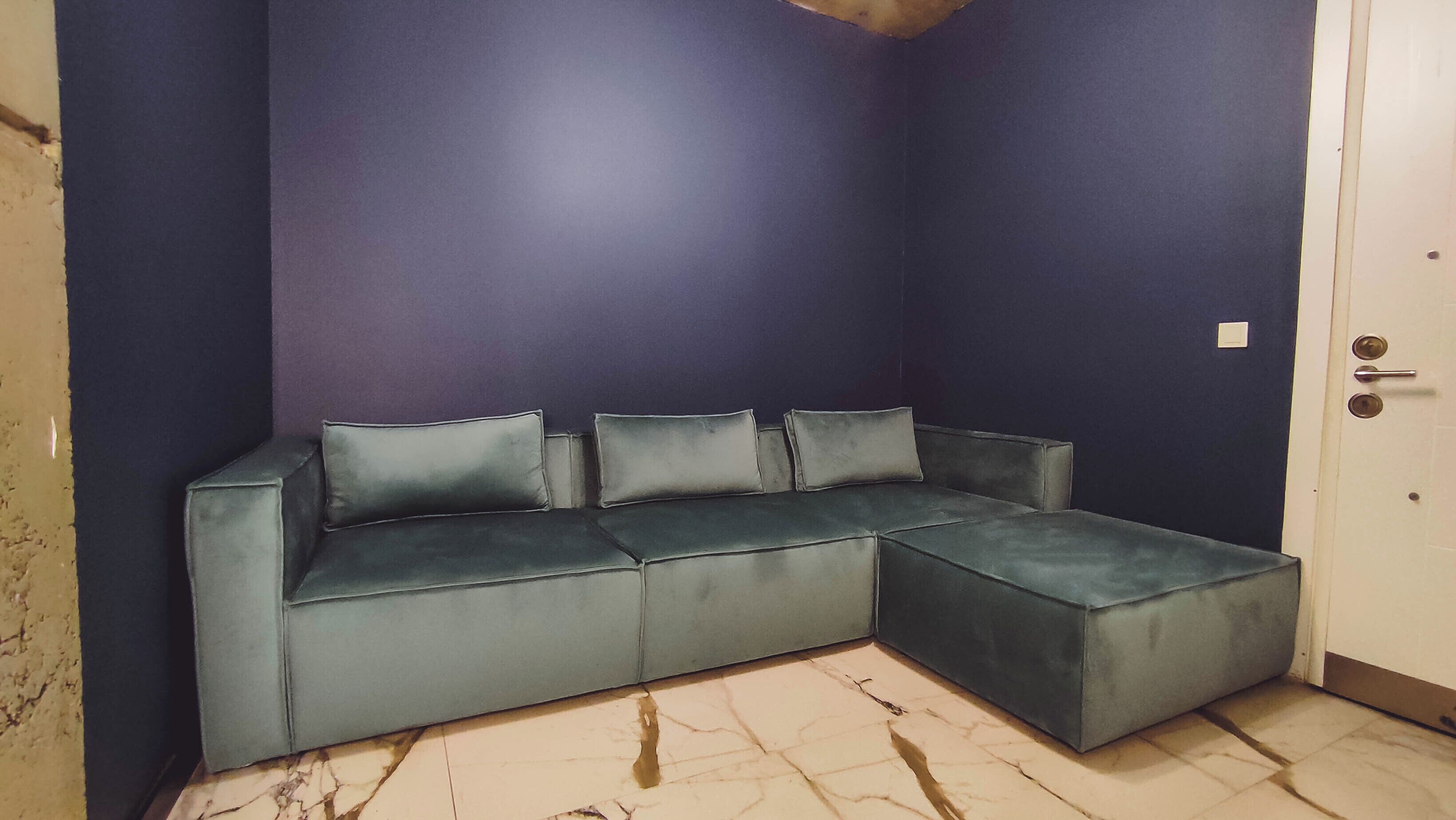 Een donkerblauwe kamer met een grijze modulaire bank en een witte deur.