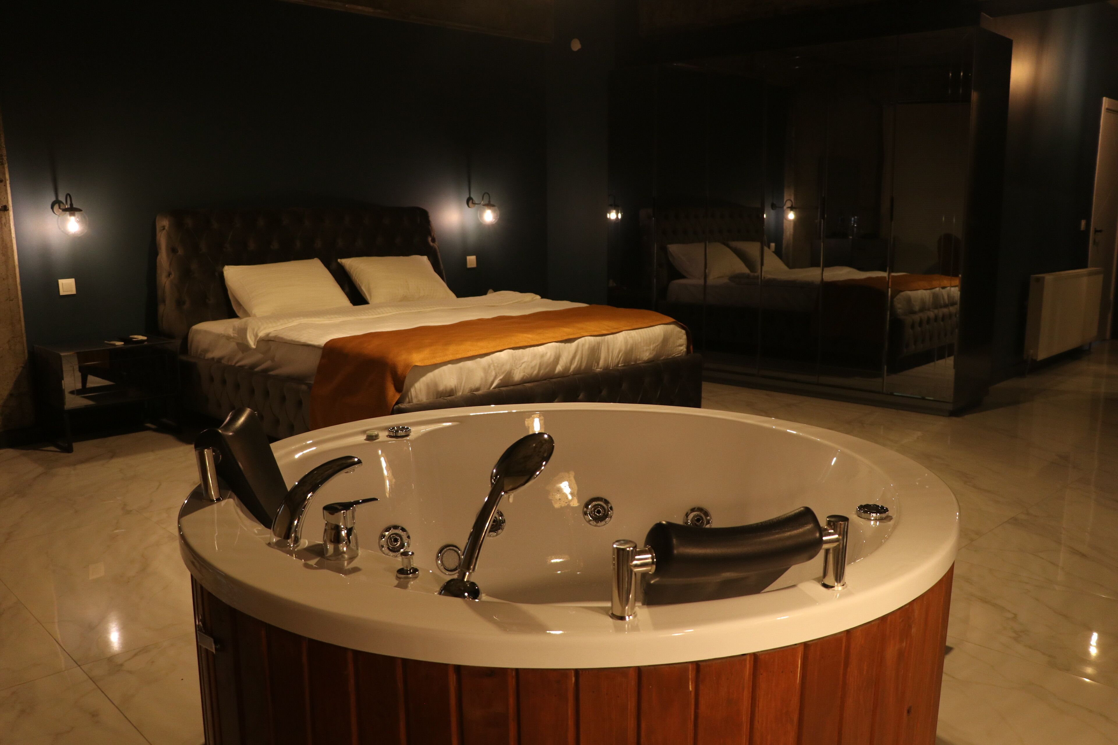 A modern bedroom with a large bed, a wooden bathtub, and a glass-enclosed walk-in closet.
