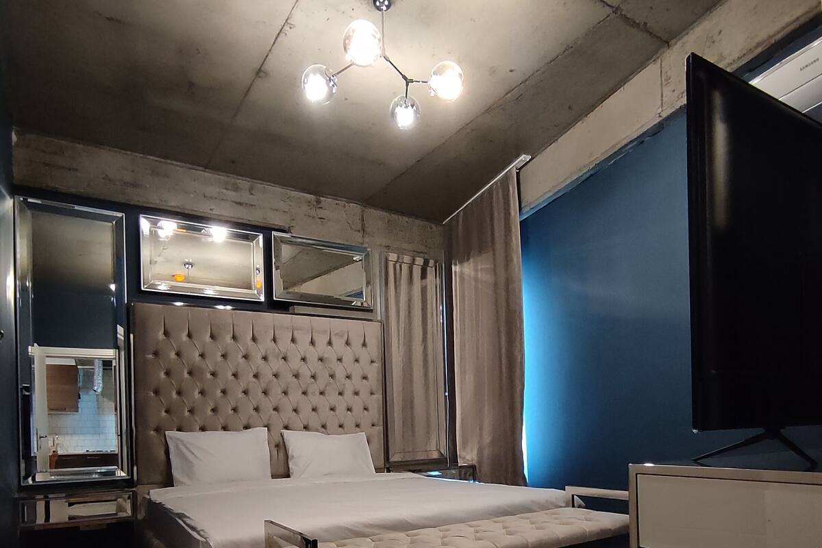 A bedroom with a bed, a TV, a mirror, and a ceiling light fixture.