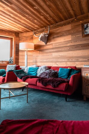 Una habitación acogedora con techo de madera, un sofá rojo con cojines de colores, una lámpara y una cabeza de ciervo montada en la pared.