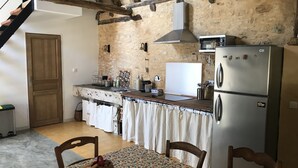 A rustic kitchen with a stone wall, wooden beams, a stainless steel refrigerator, and a dining table with chairs. - 3 Bedroom Private vacation home in Saint-Cyprien (Saint-Cyprien)
