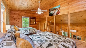 A wooden cabin bedroom with a bed, a window, a ceiling fan, and a painting of a waterfall. - Serenity Escape Treehouse on 14 Acres with easy trails, fire pit and hammock. (Fort Payne)