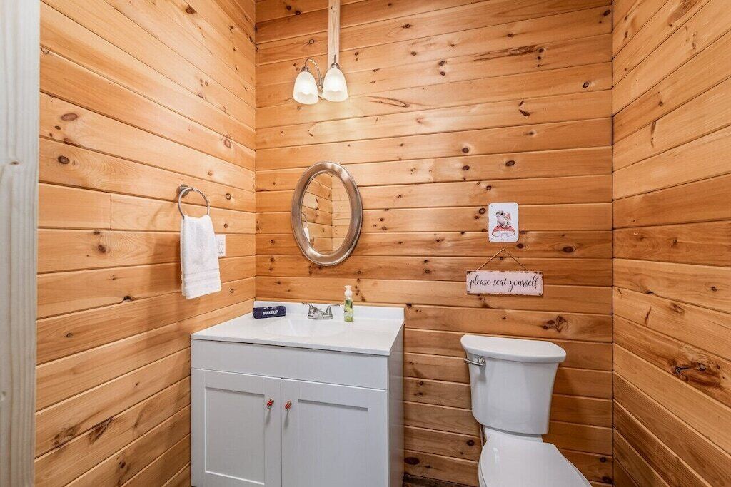 A wooden-paneled bathroom with a white sink, a mirror, a toilet, and a towel rack.