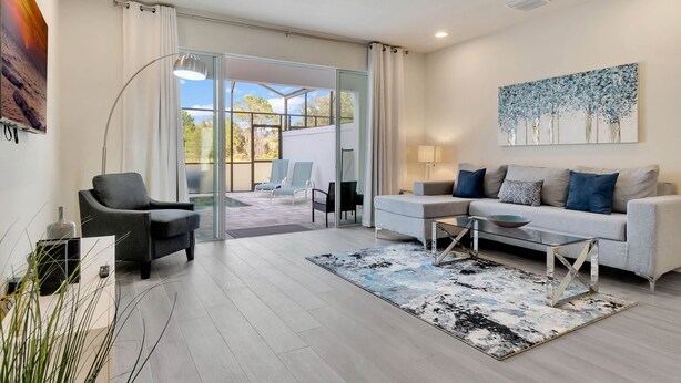 A modern living room with a sofa, armchairs, a coffee table, and a glass door leading to a balcony.