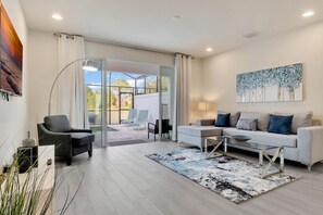 A modern living room with a sofa, armchairs, a coffee table, and a glass door leading to a balcony. - New Townhome villa located near Disney World with pool (Clermont)