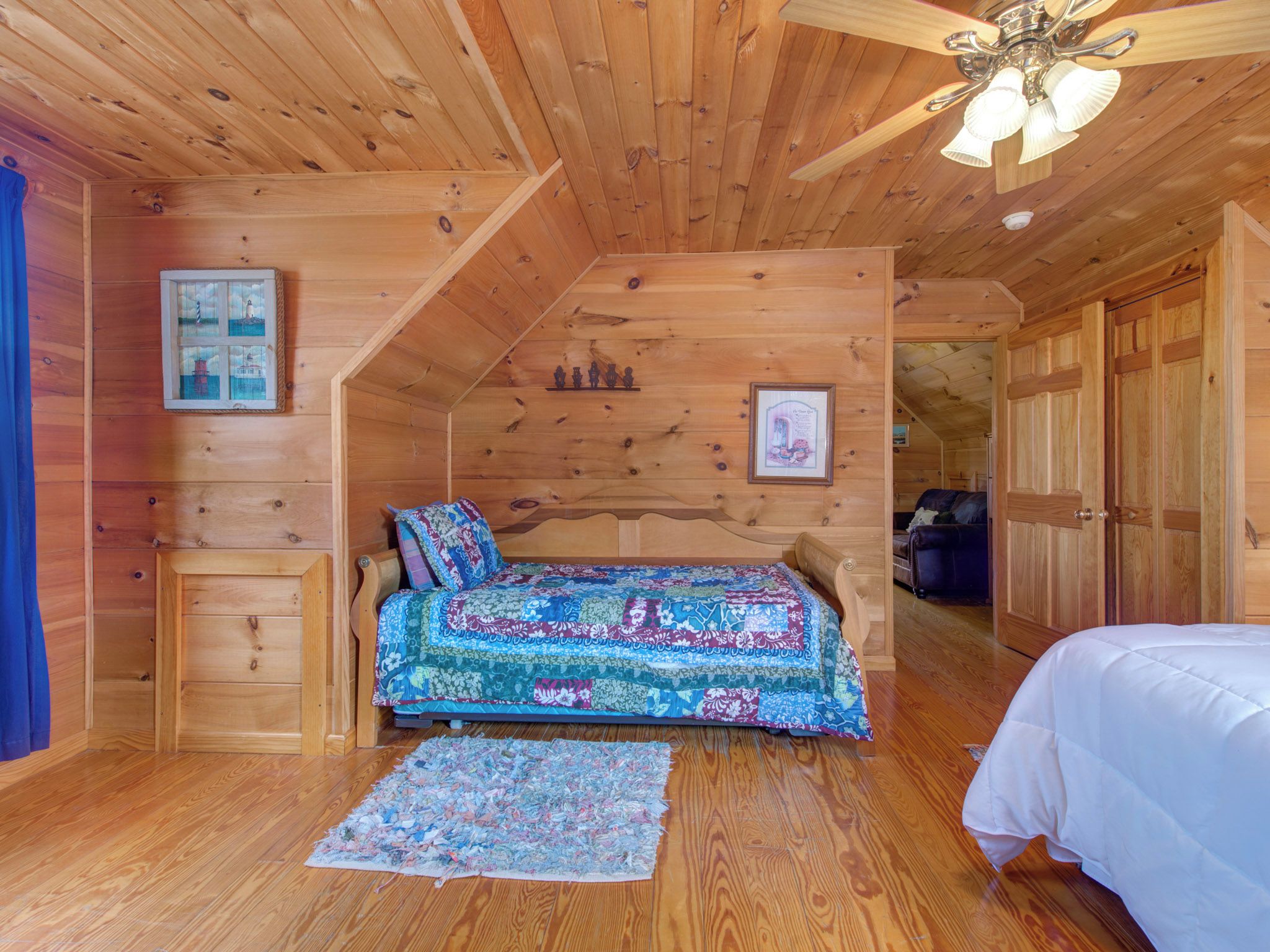 Ein gemütliches Holzblockhaus-Zimmer mit Bett, einem kleinen Beistelltisch und einem Deckenventilator.
