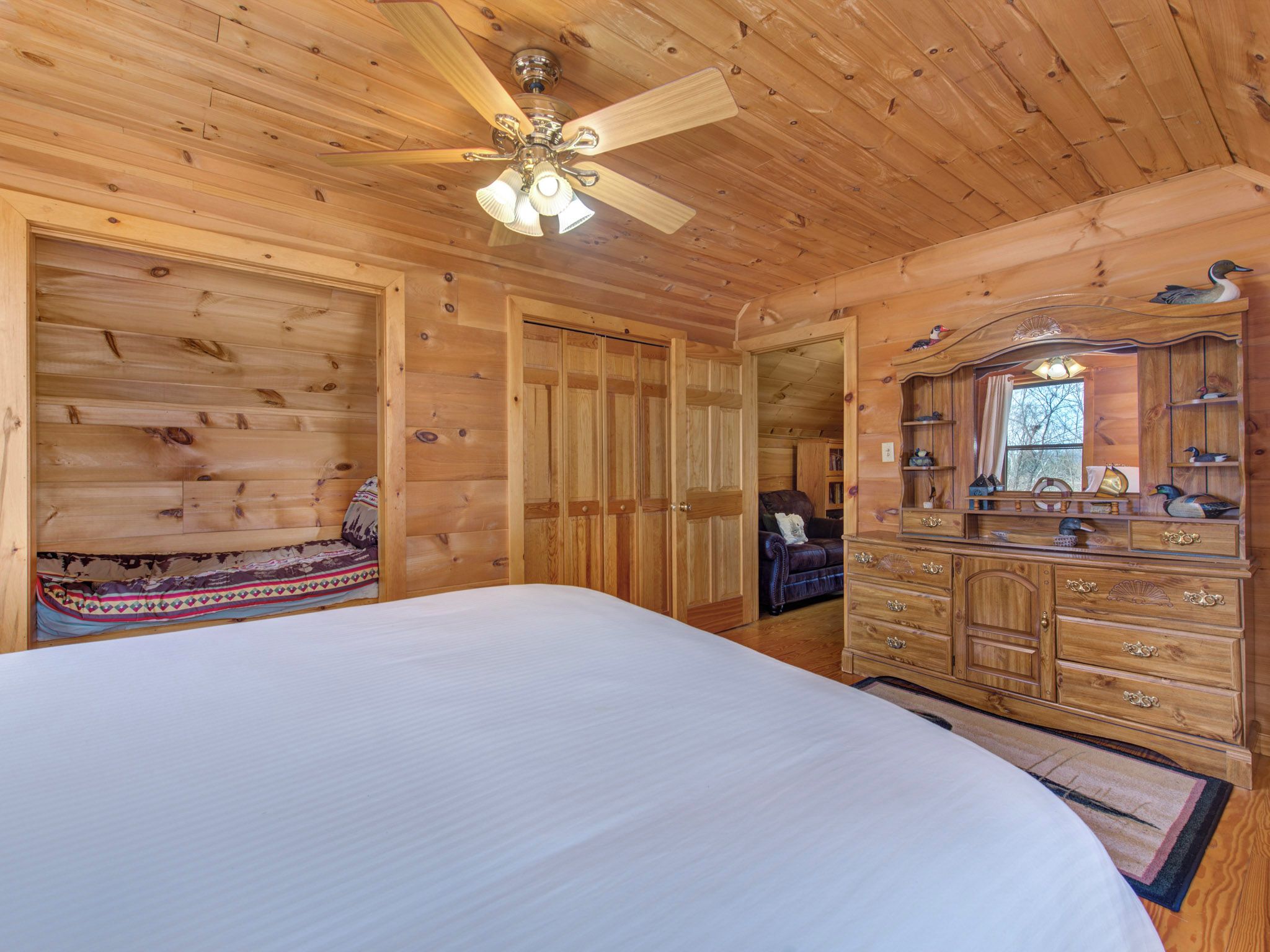 Een slaapkamer in een houten blokhut, met een bed, een kapstok en een plafondventilator.