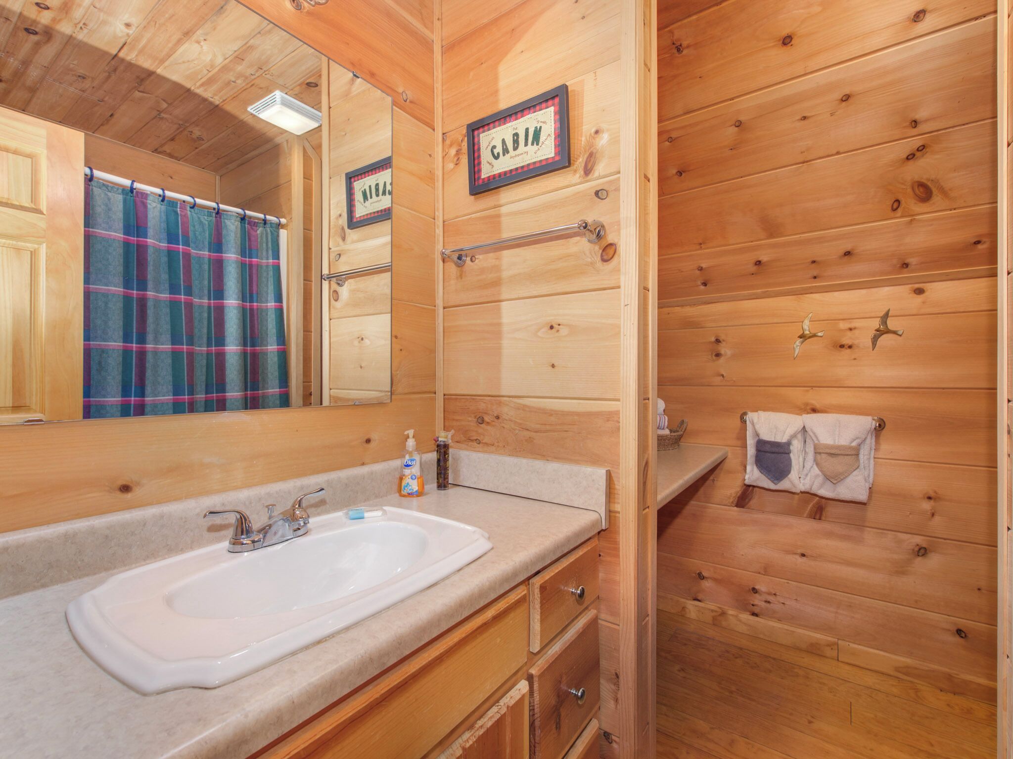 Bagno di una baita in legno con lavandino, specchio e un cartello con la scritta 'CABIN'.