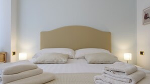 Ein ordentlich bezogenes Bett mit Kissen und gefalteten Handtüchern, eine Nachttischlampe und ein gerahmtes Bild an der Wand.