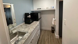 A compact kitchen with a granite countertop, stainless steel sink, black coffee maker, microwave, and a small trash bin. - Moultonborough Inn (Moultonborough)
