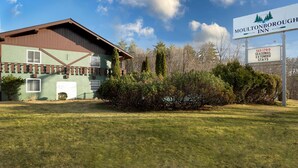A Moultonborough Inn with a green and brown building, a grassy lawn, and a clear blue sky. - Moultonborough Inn (Moultonborough)