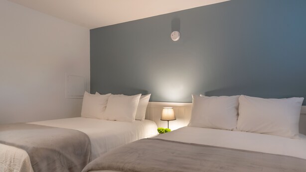 A hotel room with two beds, a nightstand with a lamp, and a wall-mounted light fixture. - Moultonborough Inn (Moultonborough)