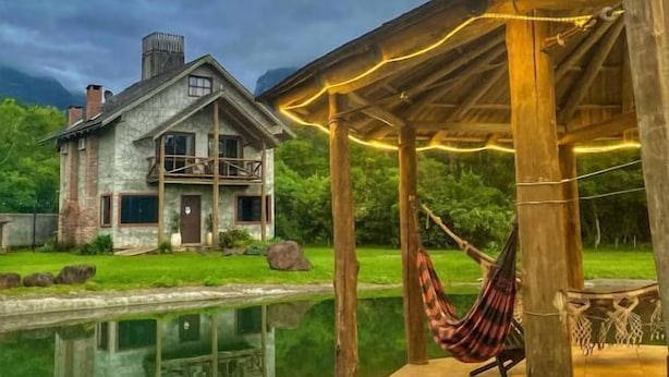 A house with a stone exterior, a wooden deck, and a hammock. - Pousada & Camping Nativos dos Canyons (Praia Grande)