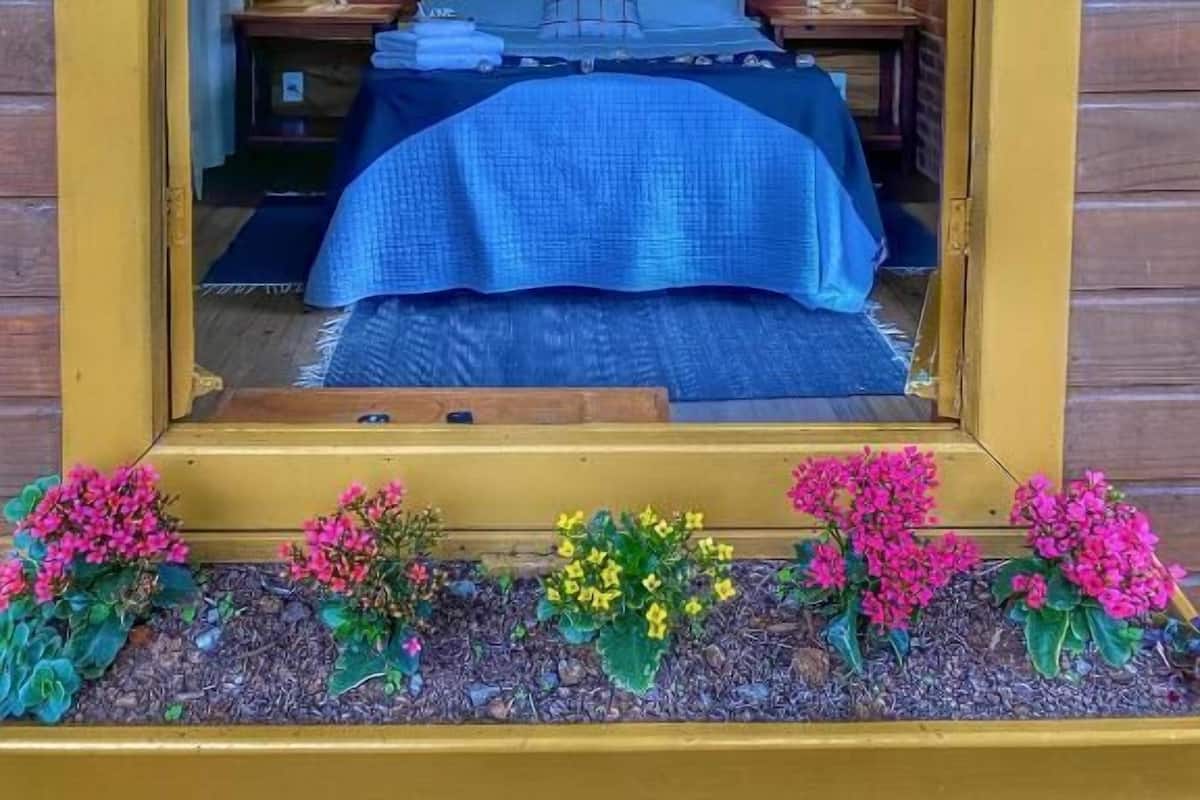 Un dormitorio de cabaña de madera con una cama, una obra de arte enmarcada, lámparas de noche y una ventana.
