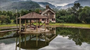 A house with a gazebo on stilts over a body of water, surrounded by mountains and greenery. - Pousada & Camping Nativos dos Canyons (Praia Grande)
