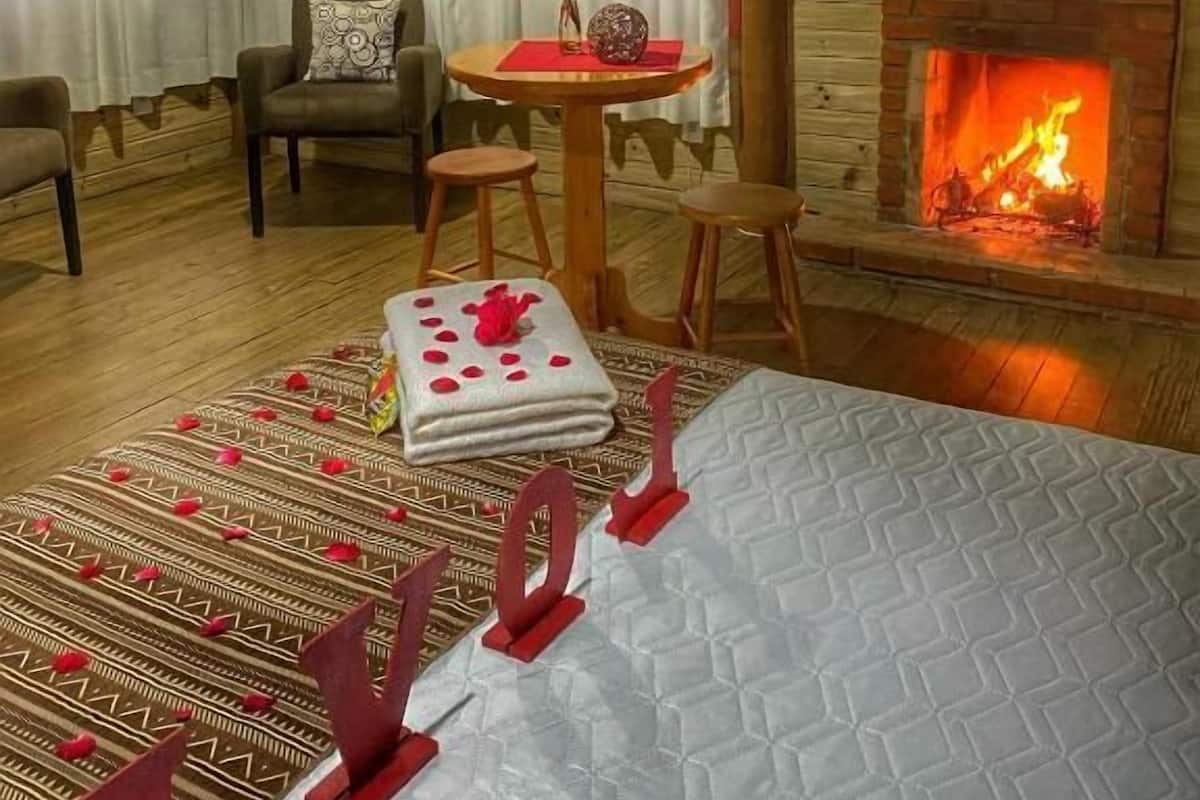 Una habitación acogedora con chimenea, un televisor montado en la pared, una mesa de comedor con sillas y una cama con cabecero decorativo.