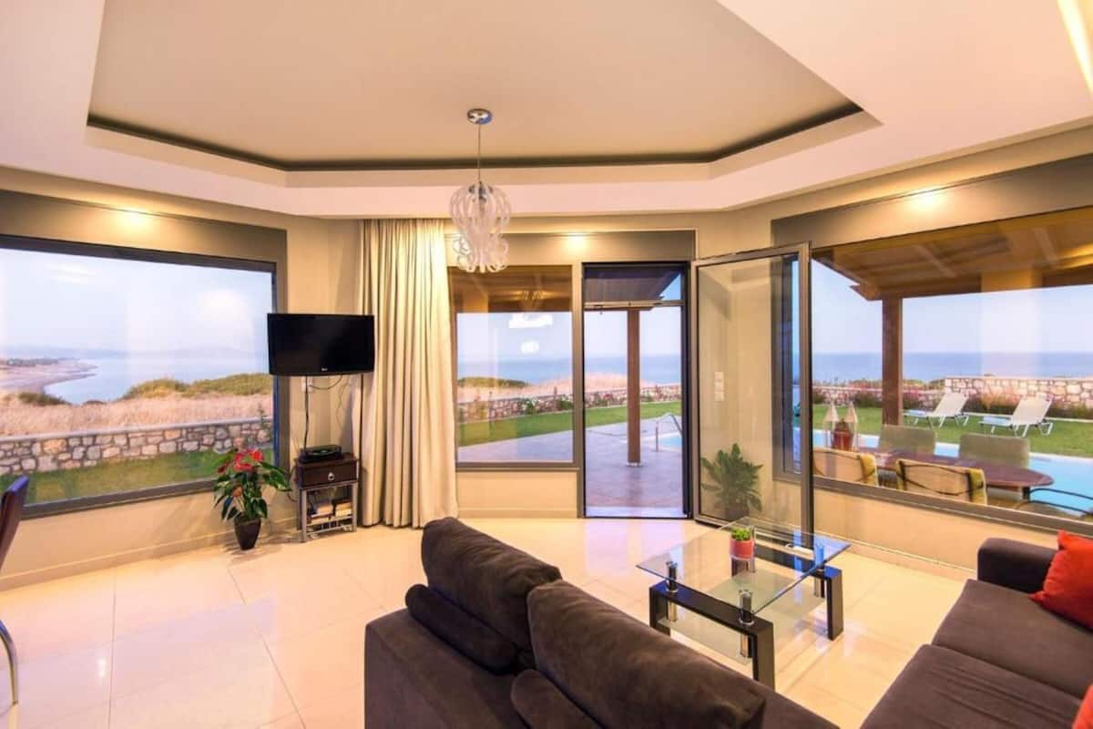 A modern living room with a large TV, comfortable seating, and a glass table.