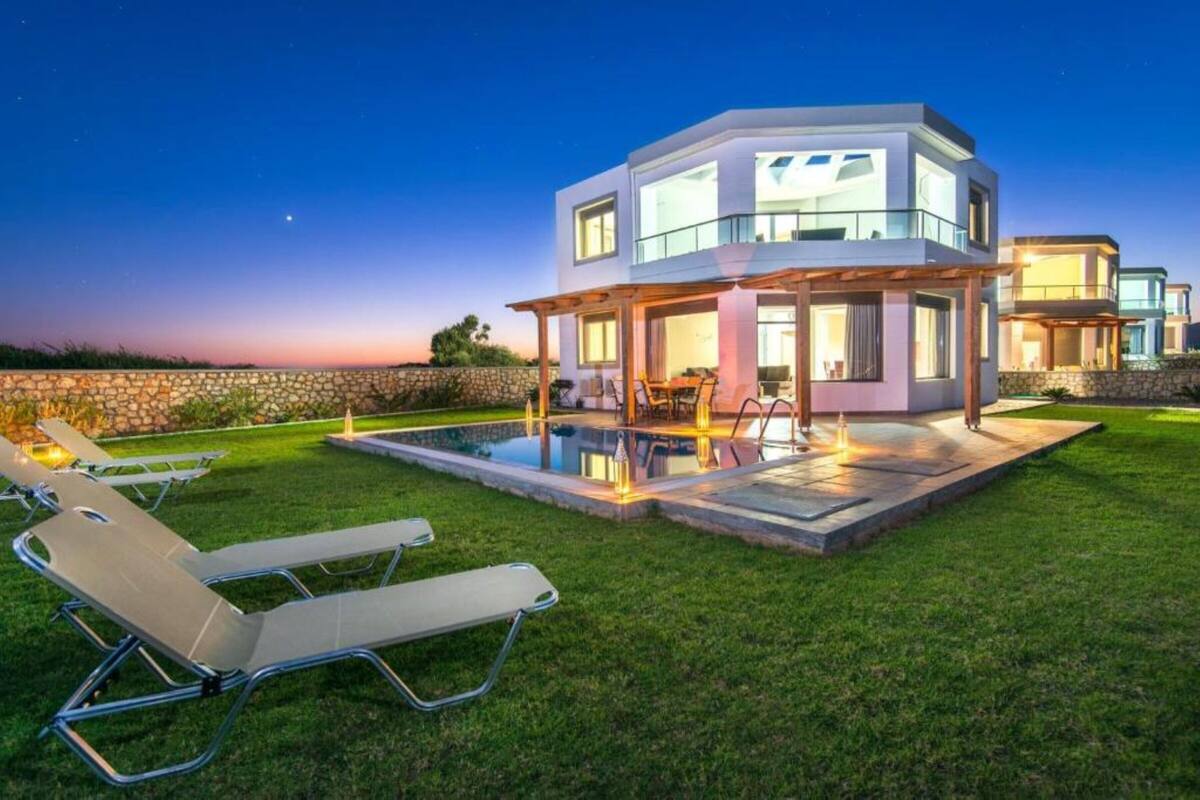 A modern house with a pool, outdoor seating, and a stone wall.