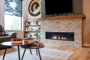 A modern living room with a fireplace, a sofa, a coffee table, and a TV mounted on the wall. - Copper Skies Lodge In Powder House Pass (South Lawrence)