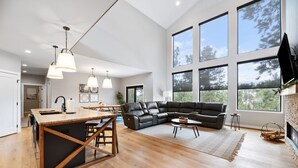 A spacious living area with a large black leather sectional sofa, a wooden dining table, and a kitchen with a marble countertop. - Copper Skies Lodge In Powder House Pass (South Lawrence)