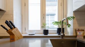 Una cocina moderna con un lavamanos de acero inoxidable, un bloque de cuchillos de madera, una planta en maceta y una bolsa de bienvenida sobre la encimera.