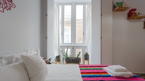 Un dormitorio con una cama, un edredón colorido y una ventana con cortinas.