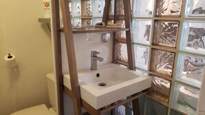 Une salle de bain avec un lavabo blanc, des toilettes et un mur en blocs de verre.