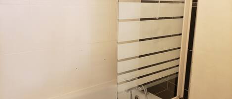 A bathroom with white tiled walls, a glass shower enclosure, and a visible drain.