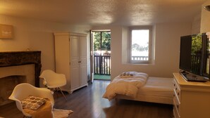 Une chambre dotée d’un lit, d’une télévision, d’une cheminée, d’une armoire et d’un balcon offrant une vue sur la verdure.