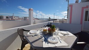 A rooftop terrace with a table set for dining, a potted plant, and a clear view of the sky. - Apartamento Alfarroba Com Terra o Vista Mar (Tavira)