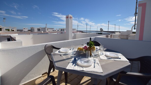 A rooftop terrace with a table set for dining, chairs, and a clear view of the cityscape. - Apartamento Alfarroba Com Terra o Vista Mar (Tavira)