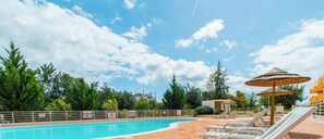 Ein Pool mit Liegestühlen und Sonnenschirmen, umgeben von Bäumen und Gebäuden.