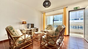 A room with wicker furniture, a television, a lamp, and a view of a balcony. - Residence Apartamento T2 com Piscina (Tavira)