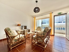 A room with wicker furniture, a television, a lamp, and a view of a balcony. - Residence Apartamento T2 com Piscina (Tavira)