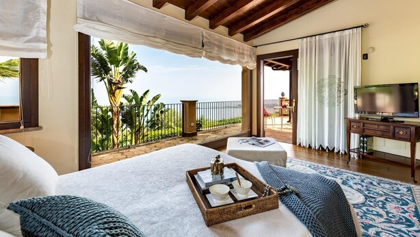 Quarto com cama grande, TV e varanda com vista para o mar.