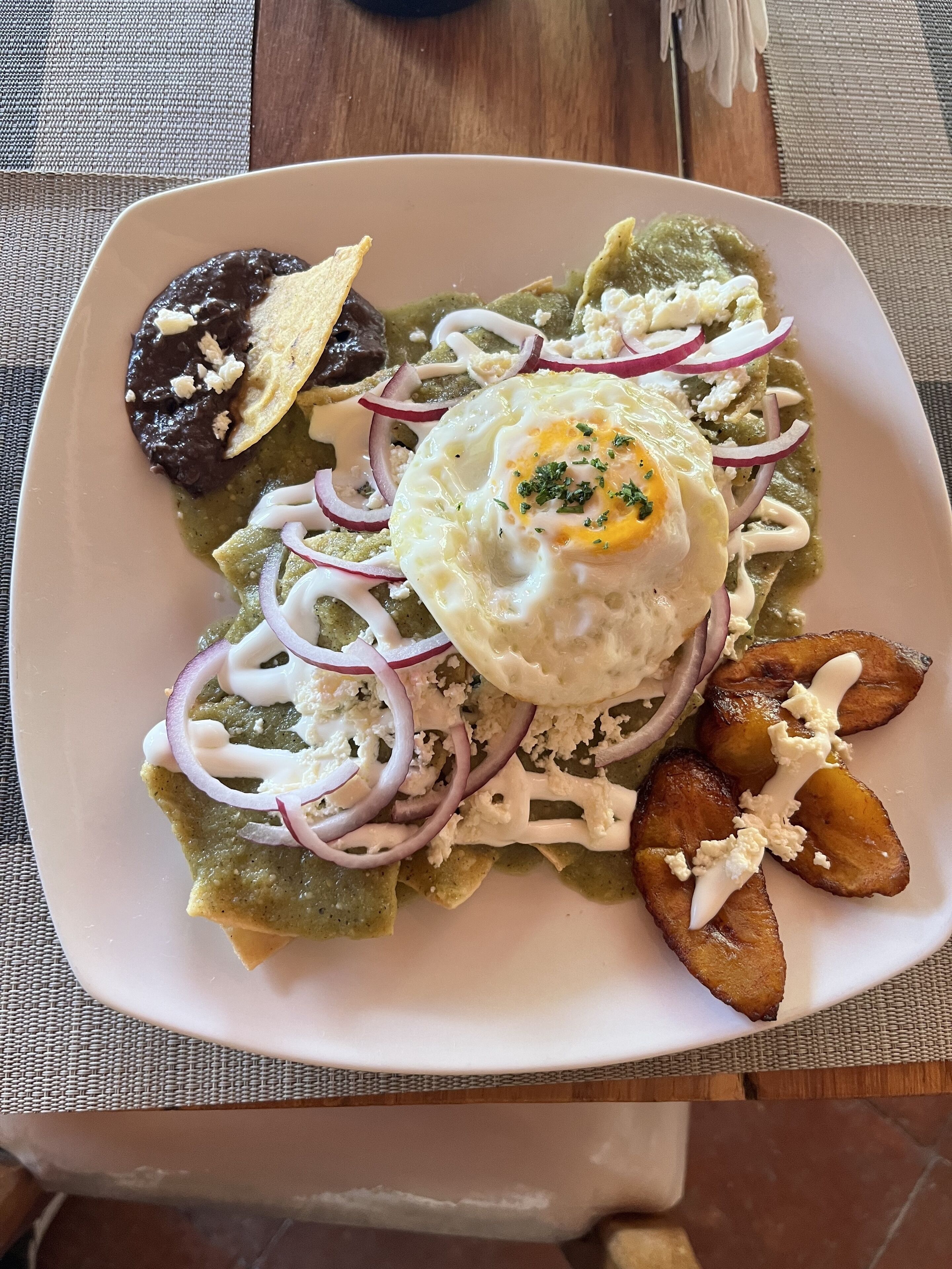 Un plato de comida con un huevo frito, cebolla roja en rodajas y una cucharada de crema.