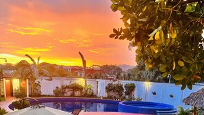 A backyard with a swimming pool, a patio with a table and chairs, and a view of a sunset. - Hotel Milin (Villa Comaltitlán)