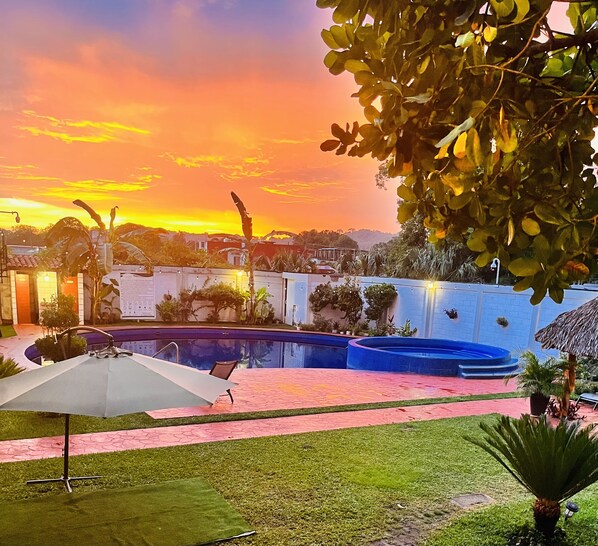 A backyard with a swimming pool, a patio with a table and chairs, and a view of a sunset. - Hotel Milin (Villa Comaltitlán)
