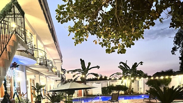 A pool area with a lounge chair and umbrella, surrounded by greenery and a building with balconies. - Hotel Milin (Villa Comaltitlán)