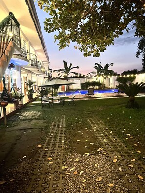 A pool area with a lounge chair and umbrella, surrounded by greenery and a building with balconies. - Hotel Milin (Villa Comaltitlán)