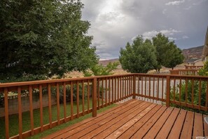 Enjoy the serene view from this deck overlooking a beautifully landscaped area with trees and a distant landscape.