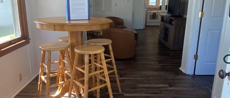A dining area with a round table and stools, a kitchen in the background, and a welcome sign on the wall.
