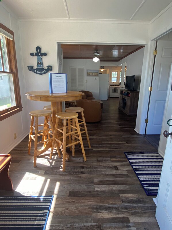 A dining area with a round table and stools, a kitchen in the background, and a welcome sign on the wall. - Cottage by the Beach (Shawano)