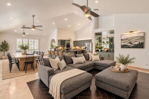 A spacious living room with a sectional sofa, a dining area, and a kitchen in the background.