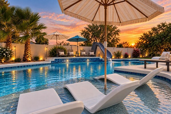 A swimming pool with lounge chairs and umbrellas, surrounded by palm trees and a sunset view. - Stunning 7bed Oasis-Pickleball,Heated Pool, hot tub, waterslide (Scottsdale)