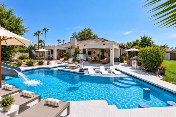 A swimming pool with lounge chairs, a basketball hoop, and a patio area with outdoor furniture.