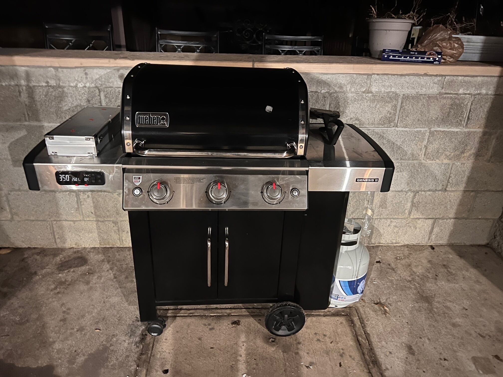 A Weber Genesis II gas grill with a digital display, three burners, and a side cabinet.