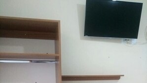 A room with a TV mounted on the wall, wooden shelves, a chair, and a toilet paper roll on one of the shelves. - Hotel Sao Luiz (Aparecida)